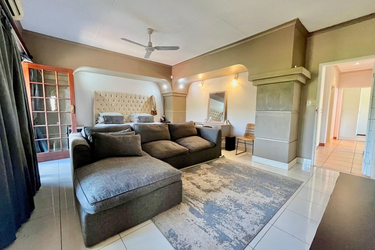 Spacious bedroom featuring tiled flooring, a ceiling fan, wall-mounted air conditioning, and a unique built-in architectural alcove for the bed area.