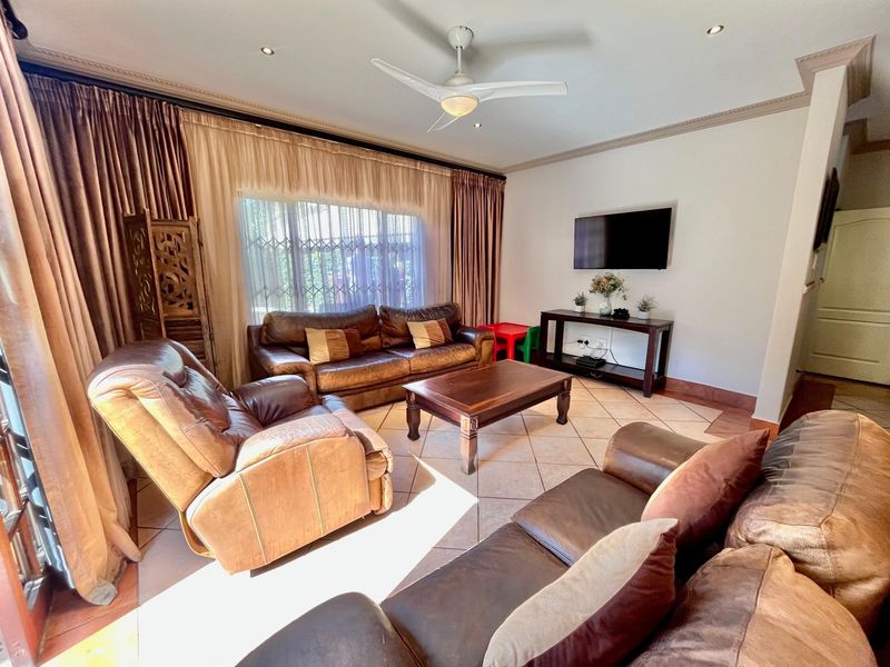 A well-maintained living room featuring tiled flooring, recessed lighting, and a ceiling fan, with large windows covered by curtains.