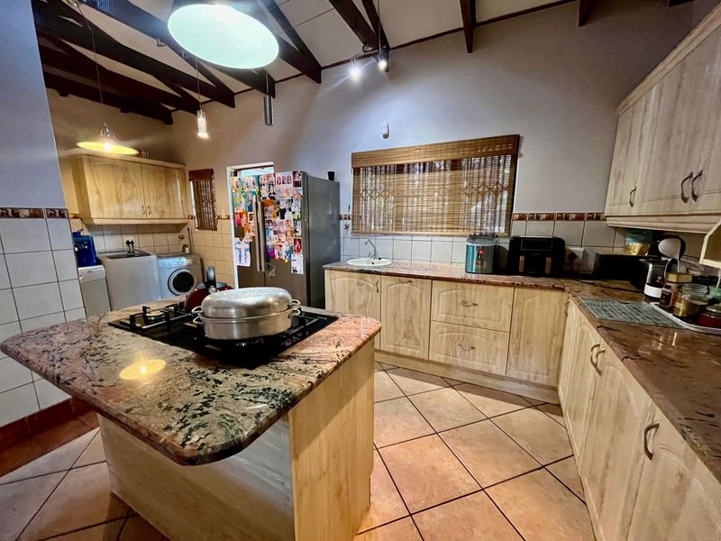 Spacious kitchen featuring granite countertops, a central island with a gas hob, ample cabinetry, and exposed timber beams under a vaulted ceiling.