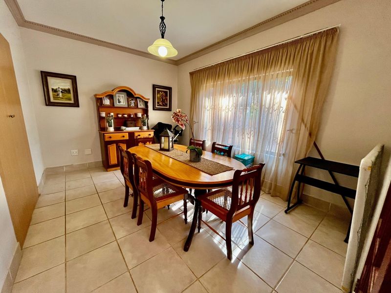 A functional dining room featuring ceramic floor tiles, coved ceiling cornicing, and a large window allowing natural light into the space.