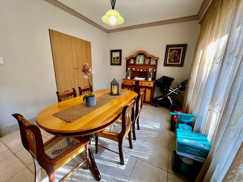 A dining room featuring tiled flooring, a built-in cupboard, and decorative ceiling cornicing, providing a functional space for family meals.