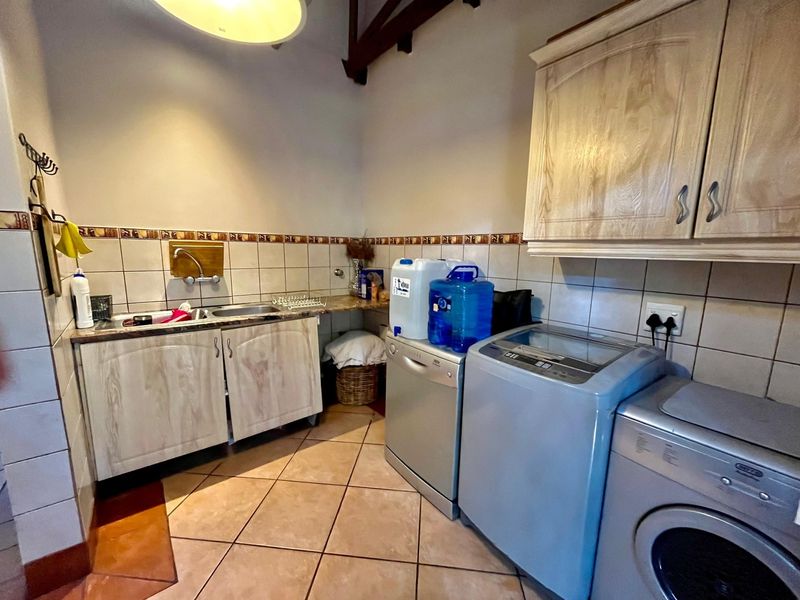 Functional laundry room featuring built-in cabinetry, tiled backsplash, stainless steel sink, and exposed timber ceiling beams.