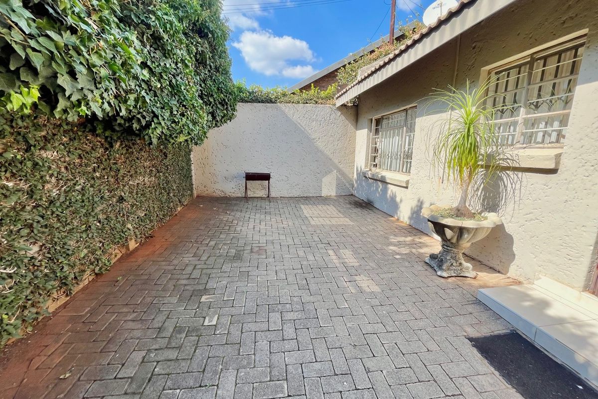 A private rear courtyard featuring paved flooring, high boundary walls with climbing ivy, and security bars on the windows.