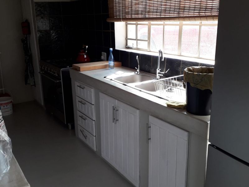 A functional kitchen featuring white cabinetry, a double basin sink, tiled backsplash, and a freestanding stove, with natural light from a window.