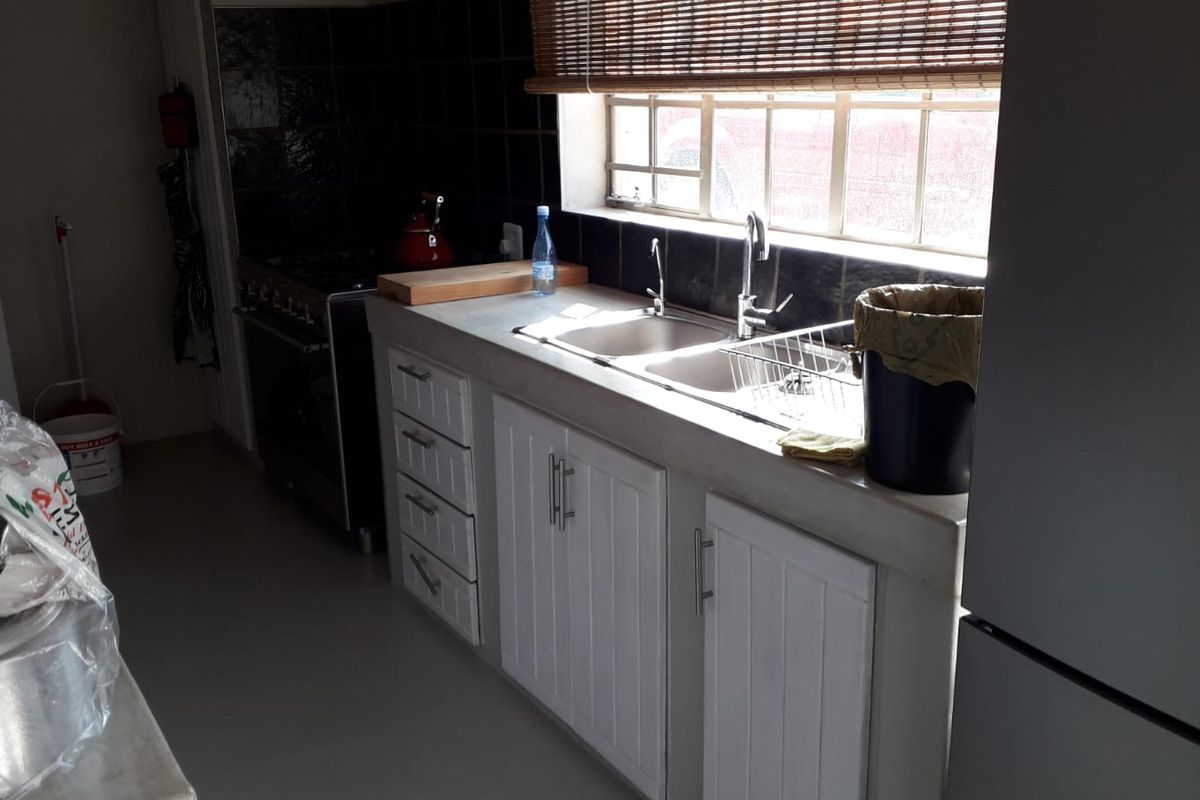 A functional kitchen featuring white cabinetry, a double basin sink, tiled backsplash, and a freestanding stove, with natural light from a window.
