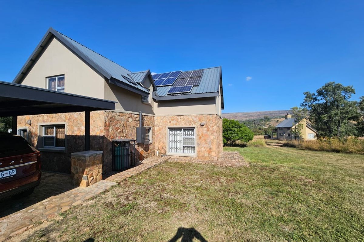 Rear view of a modern house featuring stone cladding, a metal roof with solar panels, a carport, and a paved walkway leading to the garden.
