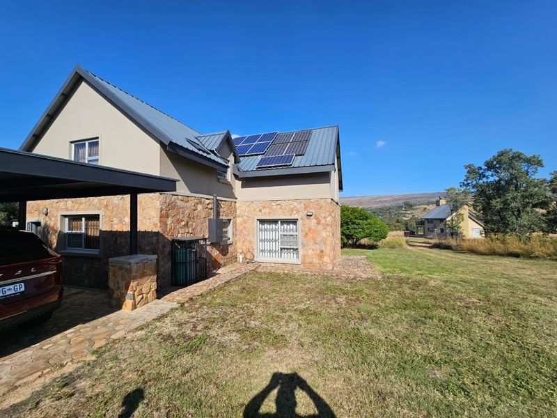 Rear view of a modern house featuring stone cladding, a metal roof with solar panels, a carport, and a paved walkway leading to the garden.