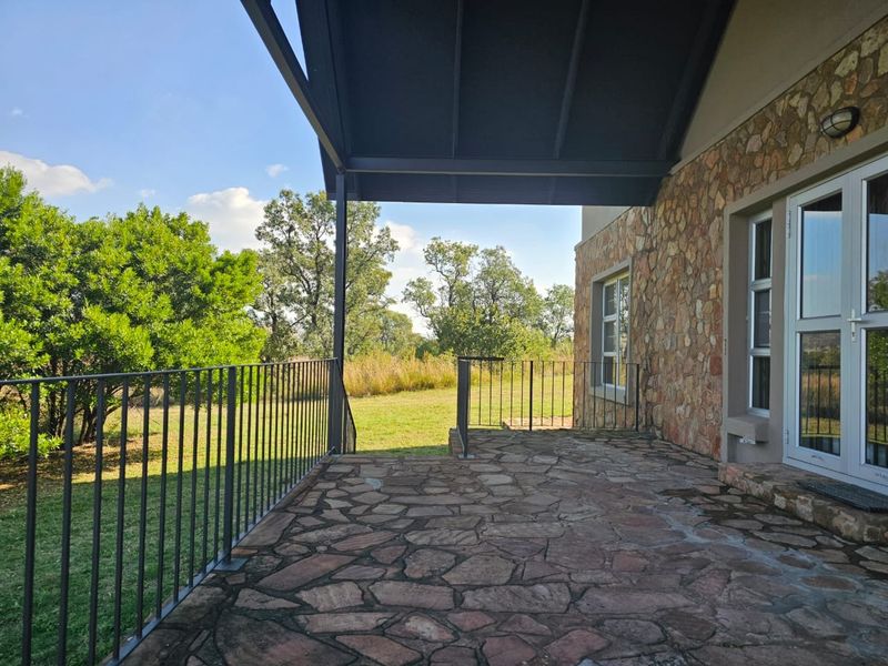 A covered patio featuring flagstone flooring, stone-clad exterior walls, and metal railings, overlooking a spacious garden area.