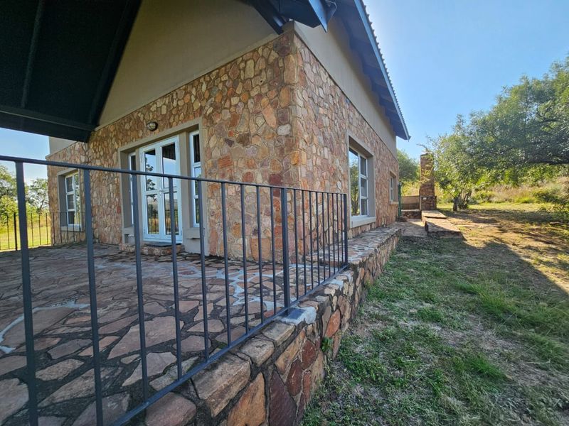 A spacious outdoor patio featuring natural stone cladding, stone paved flooring, a metal safety railing, and an integrated outdoor fireplace.