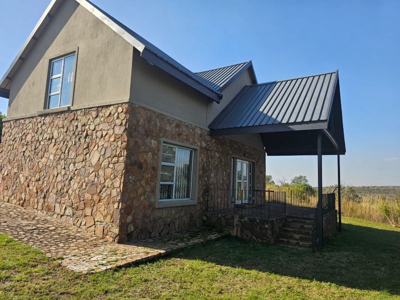 Rear view of a house featuring stone cladding, a metal roof, and a covered patio area overlooking the surrounding landscape.