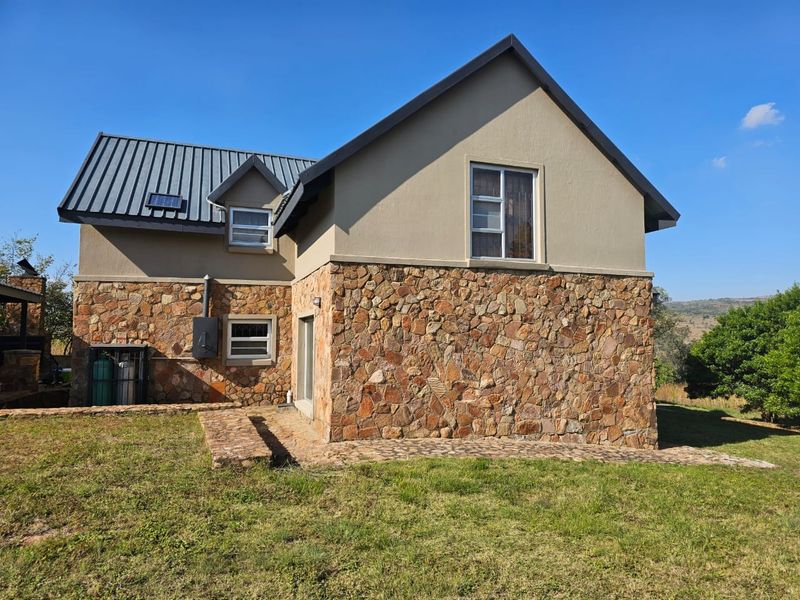 Rear view of a double-story house featuring stone cladding, a metal roof, and a stone-paved walkway leading to the garden.