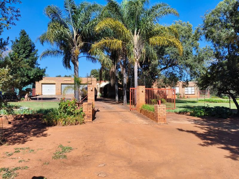 Front view of a farm property featuring a brick driveway, gated entrance, double garage, and established trees.