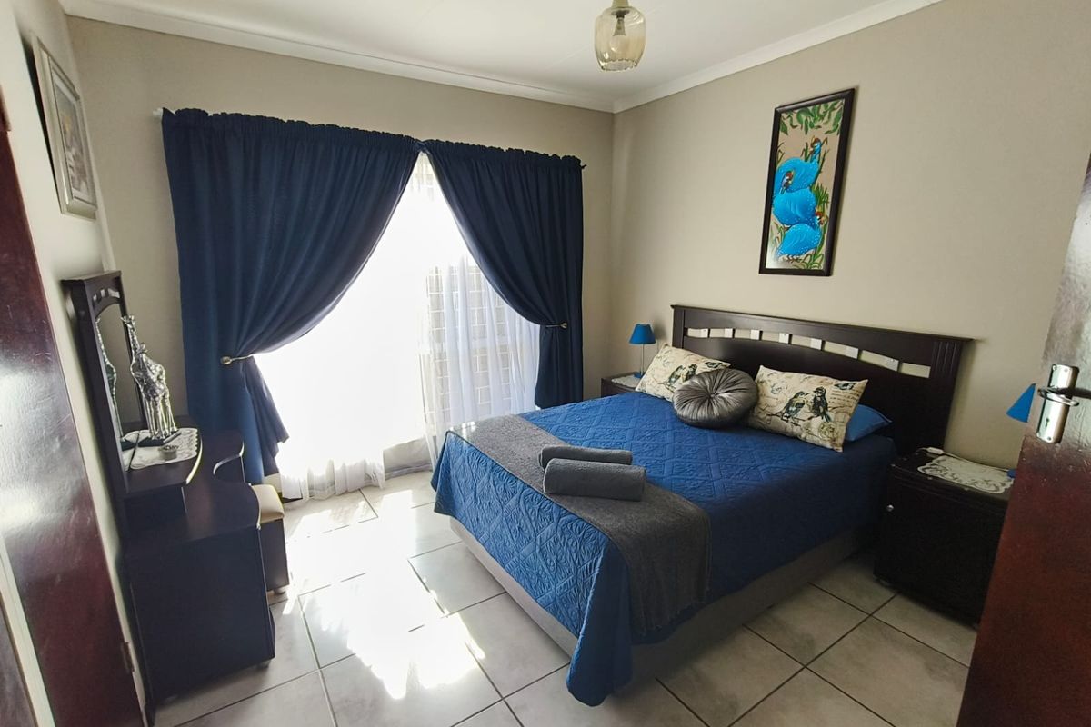 A well-maintained bedroom featuring neutral wall tones, tiled flooring, and a sliding door providing natural light.