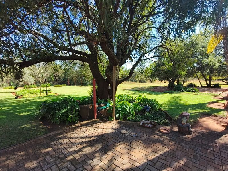 A well-maintained garden area featuring mature trees, lush green lawn, and brick-paved patio space, providing a serene outdoor setting on the farm property.