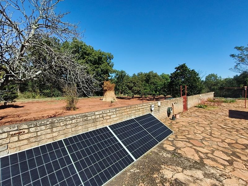 Outdoor garden area featuring a stone paved patio, brick boundary wall, and ground-mounted solar panels set against a rural landscape.