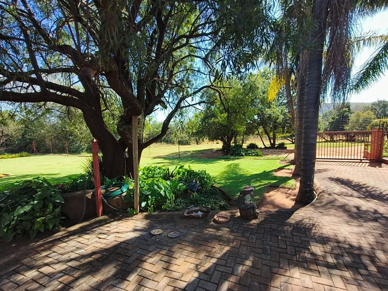 A well-maintained farm garden featuring mature trees, expansive lawn areas, and a paved driveway leading to a secure gated entrance.