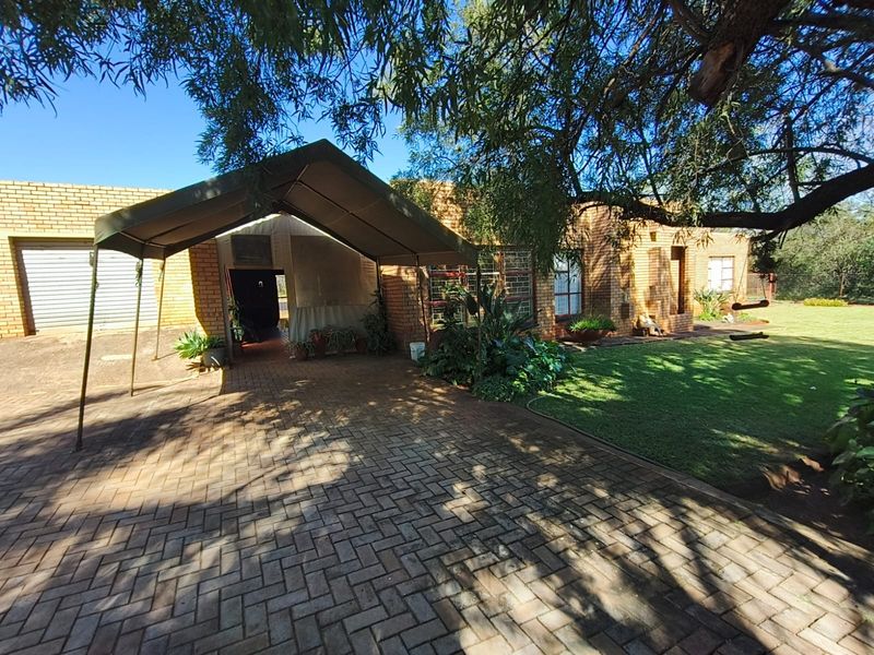 Front exterior view of a brick farmhouse featuring a paved driveway, a covered carport, and a well-maintained lawn area.