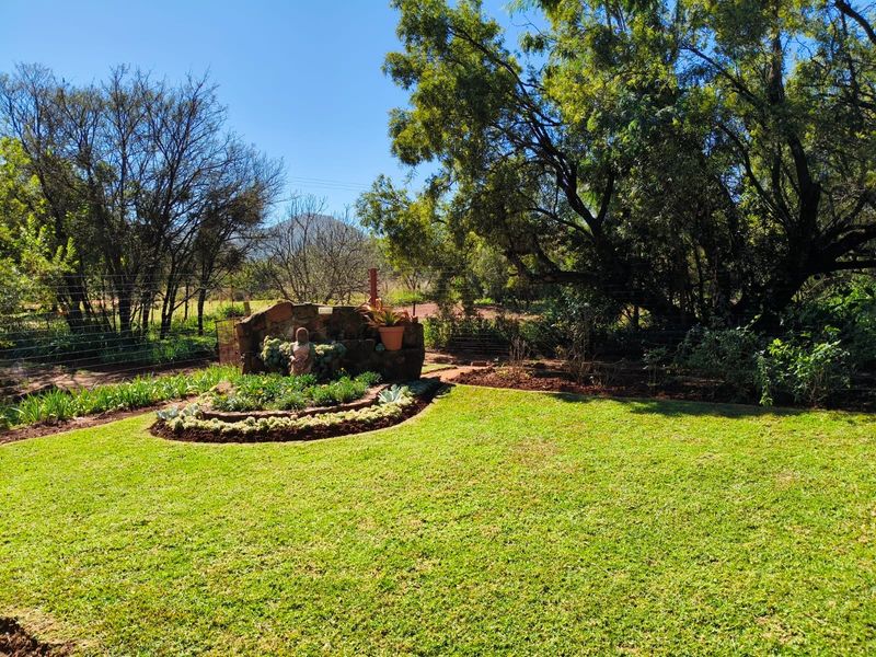 A well-maintained garden area featuring a stone retaining wall, landscaped flower beds, and mature trees on a farm property.