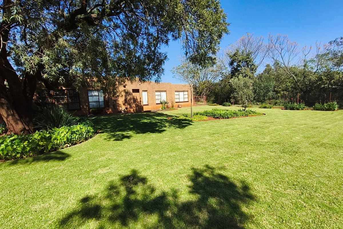 A spacious rear garden featuring a well-maintained lawn, mature trees, and a face brick building facade with security bars on the windows.