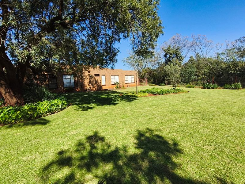 A spacious rear garden featuring a well-maintained lawn, mature trees, and a face brick building facade with security bars on the windows.
