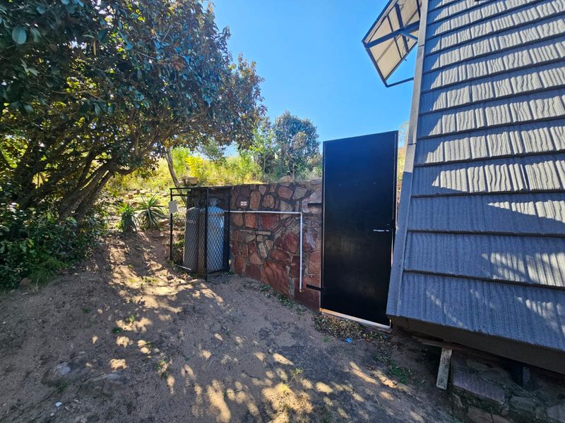 Rear exterior view showing a stone-clad wall, gas cylinder storage cage, and a metal access door adjacent to the building structure.