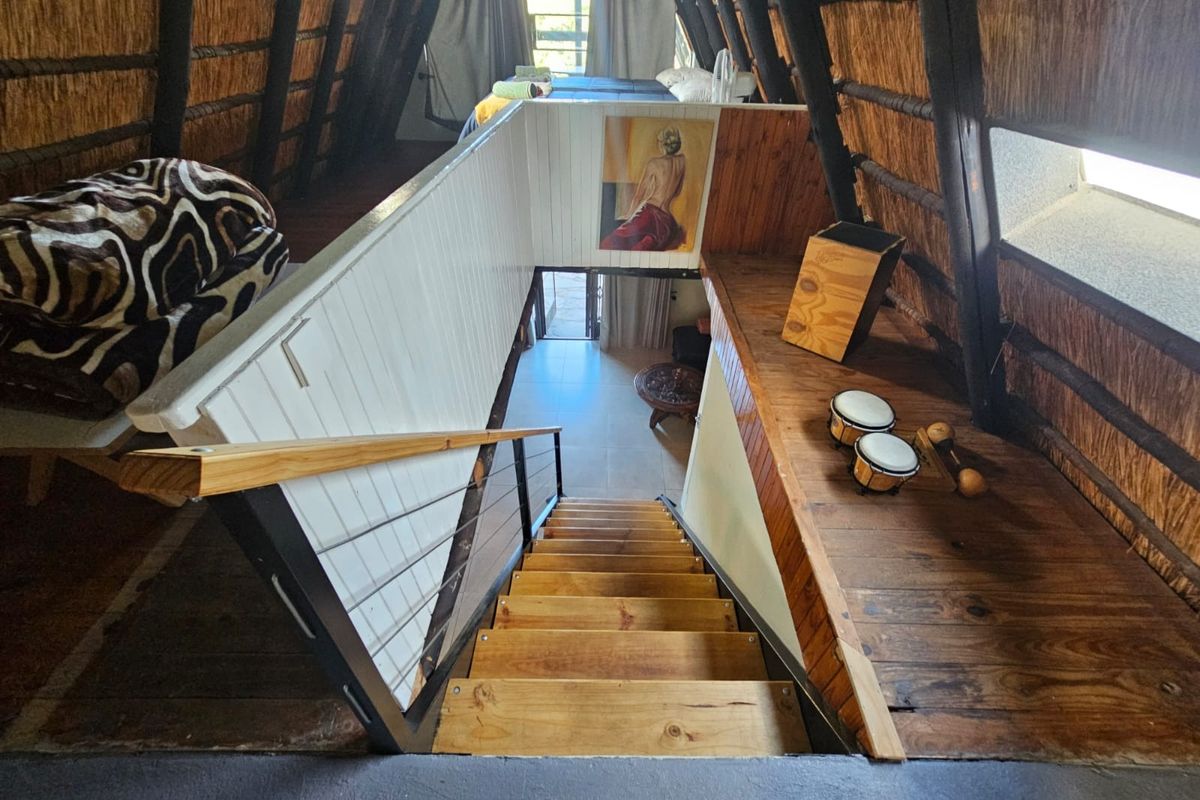 Loft-style bedroom featuring exposed timber rafters, a thatched roof, and a wooden staircase leading to the lower level.