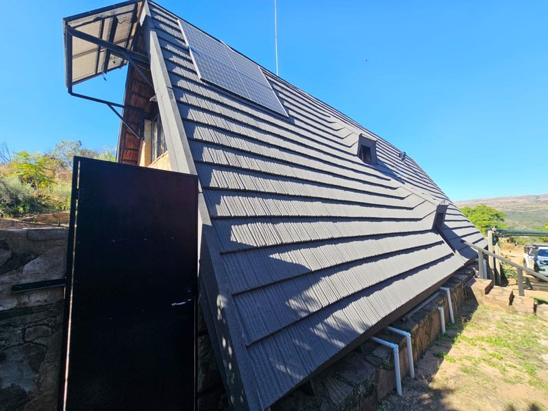 Rear view of an A-frame style house featuring a tiled roof with integrated solar panels and stone foundation base.