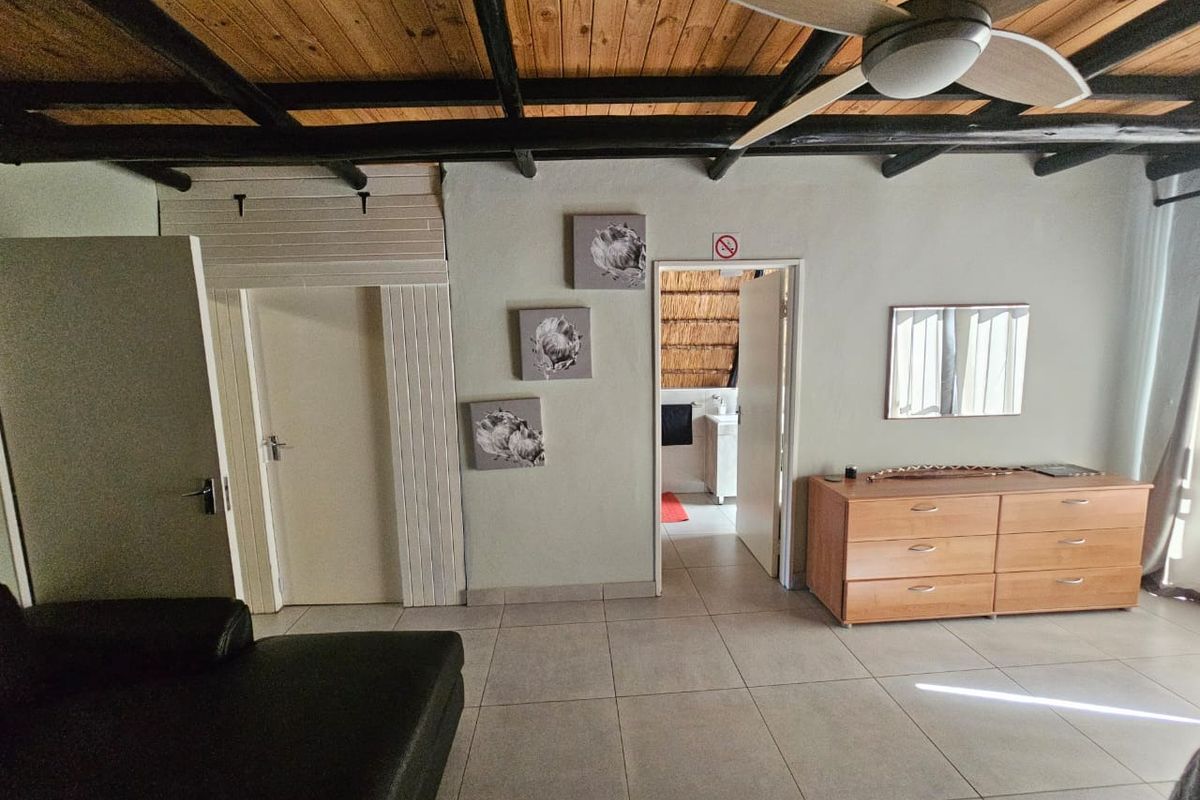 Living area featuring exposed timber beam ceilings, ceiling fan, and neutral tiled flooring, with direct access to an adjoining room.