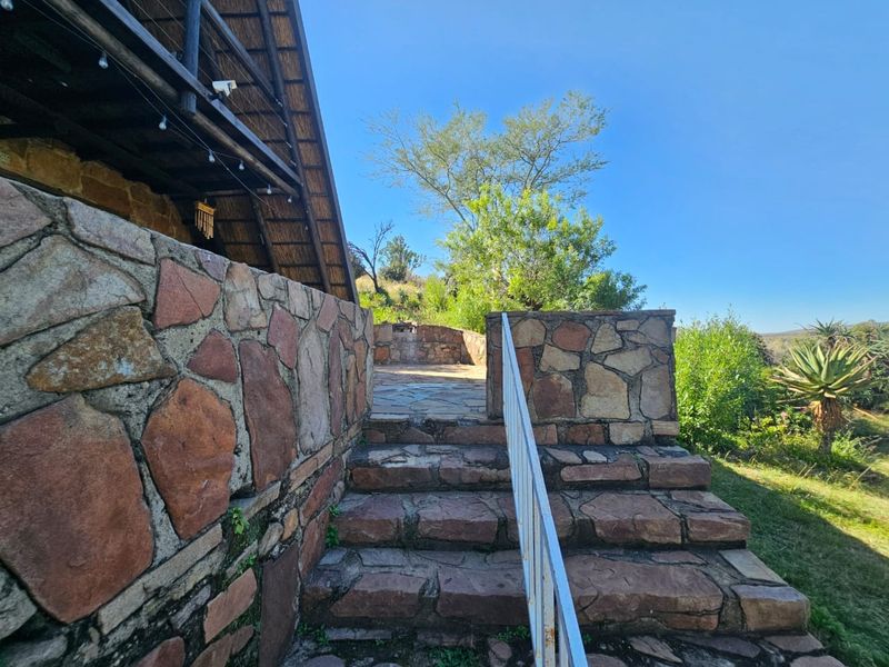Outdoor stone staircase leading to a patio area with stone cladding and a metal handrail, set against a natural landscape.