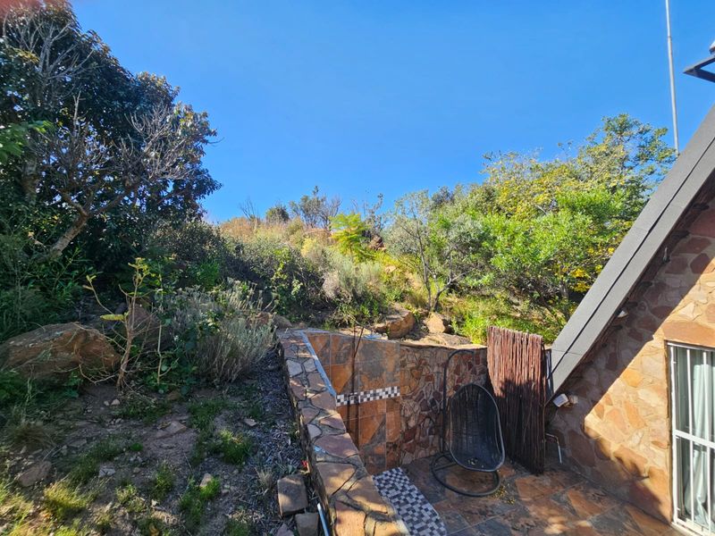 An outdoor area featuring stone-clad walls, a built-in shower, and tiled flooring, set against a natural hillside garden backdrop.