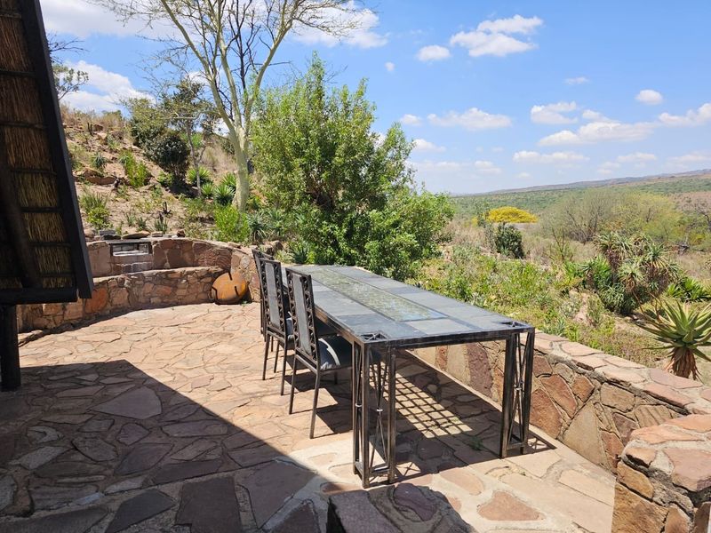 An outdoor stone-paved patio featuring a built-in stone braai and expansive views of the surrounding natural landscape.