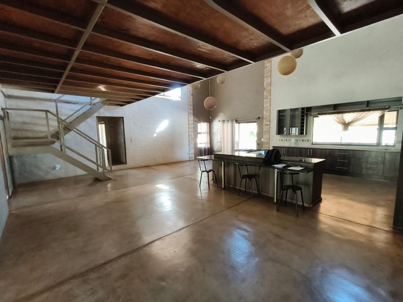 Spacious open-plan living and kitchen area featuring polished concrete floors, exposed timber ceilings, a modern kitchen island, and a striking stone feature wall.