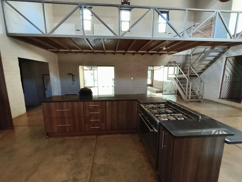 Spacious open-plan kitchen area featuring a large island with gas cooktop, concrete flooring, and a mezzanine level with metal staircase.