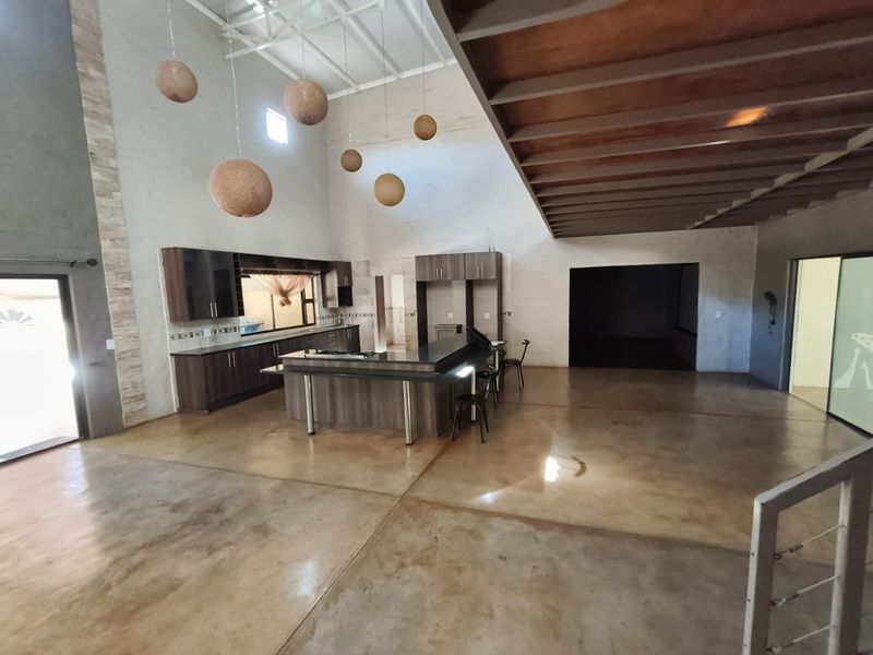 Spacious open-plan living and kitchen area featuring polished concrete floors, vaulted ceilings with exposed timber beams, and a modern kitchen island.