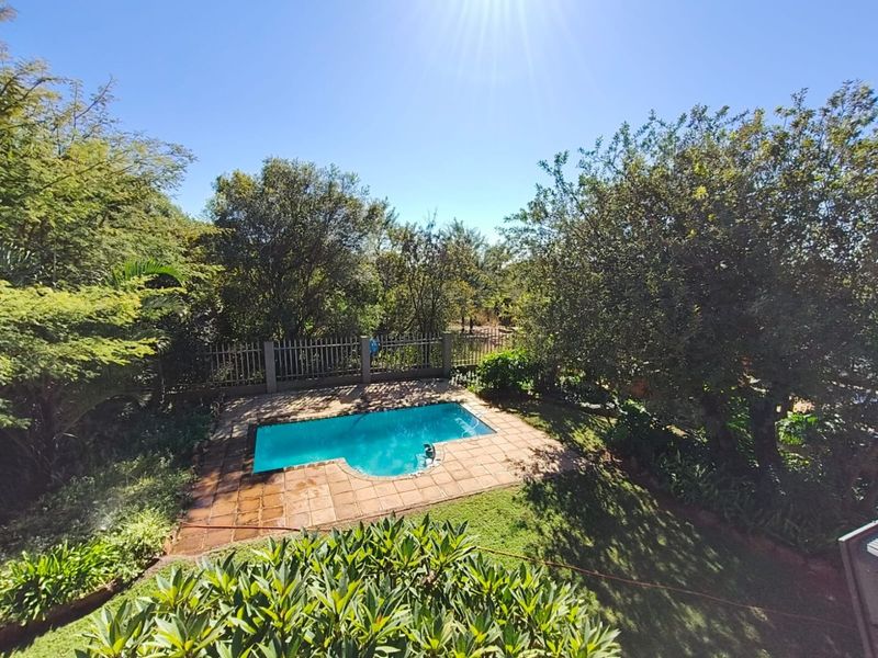 An elevated view of a private swimming pool set within a landscaped garden, featuring a tiled surround and perimeter fencing.