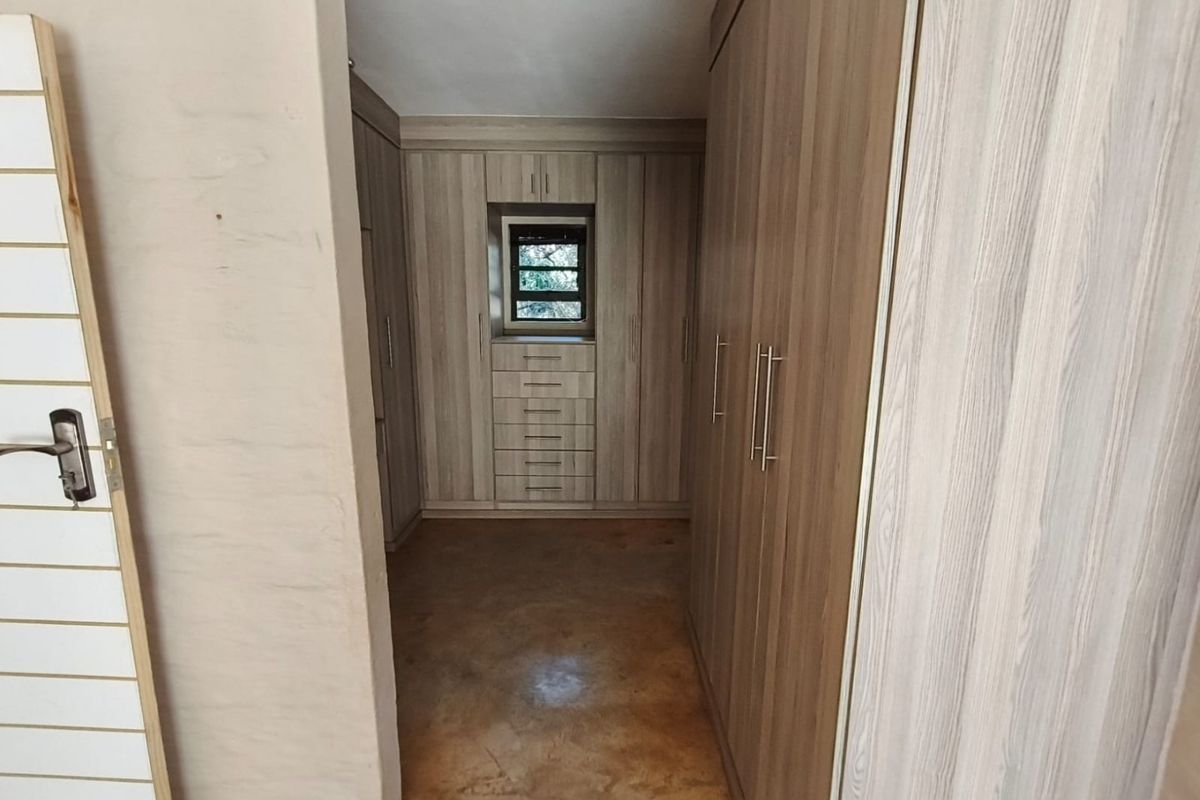 A walk-in dressing area featuring extensive built-in wooden cabinetry with integrated drawers and a small louvered window for natural light.