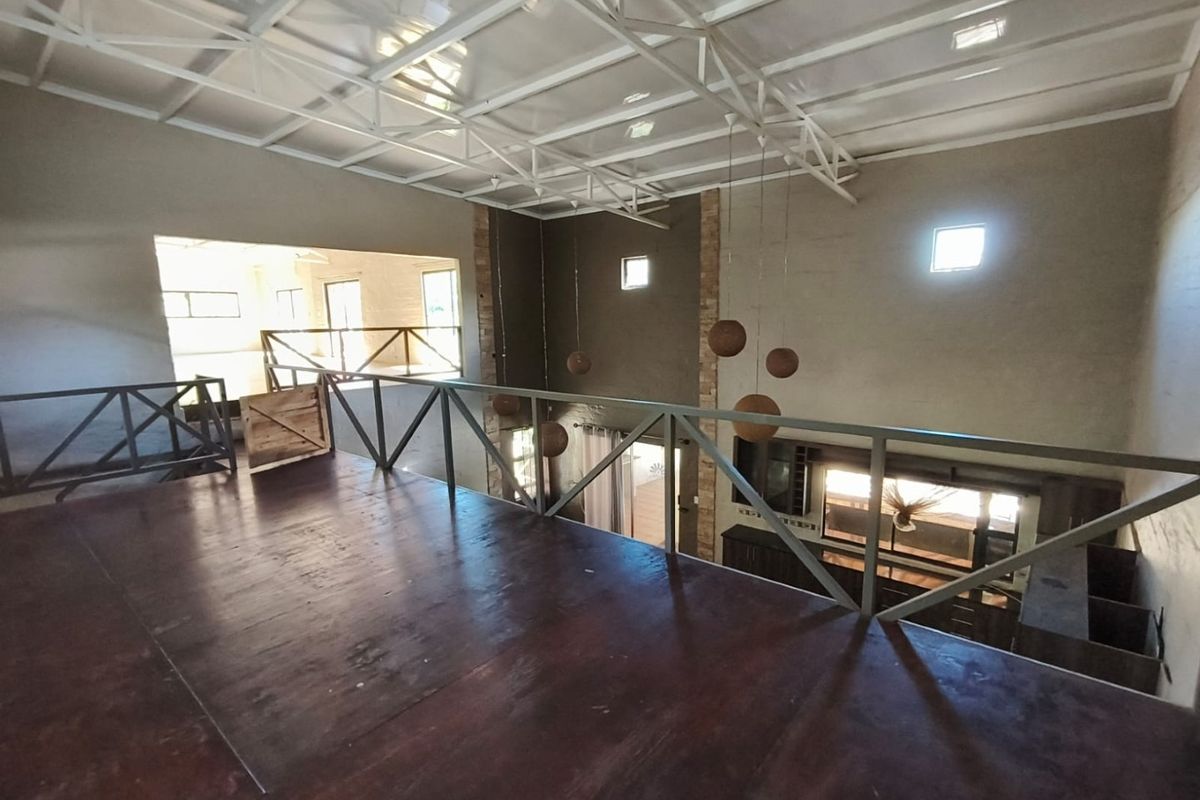 Spacious mezzanine level featuring exposed steel roof trusses, timber flooring, and a metal balustrade, offering an open-plan view overlooking the lower living area.