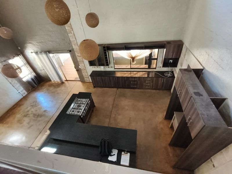 Spacious open-plan kitchen and living area featuring polished concrete floors, modern dark wood cabinetry, and a built-in gas hob under a high vaulted ceiling.