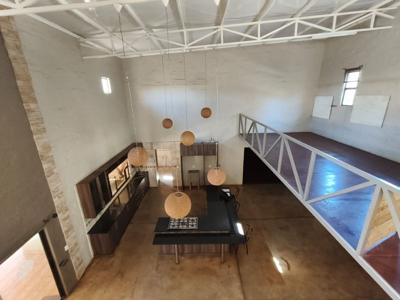 Spacious open-plan living area featuring a modern kitchen with island, gas hob, exposed steel roof trusses, and a mezzanine level overlooking the main floor.