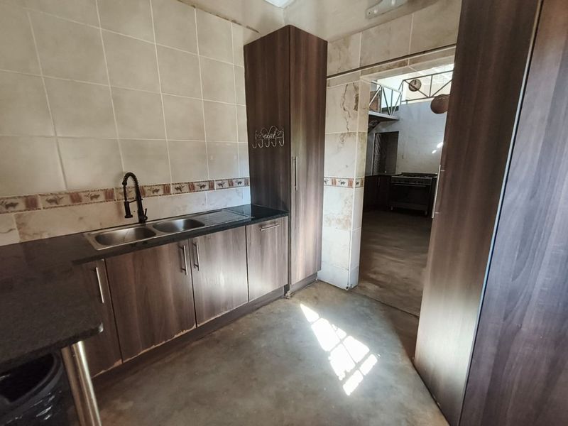 A functional scullery area featuring dark laminate cabinetry, granite countertops, and a double bowl sink, with visible wear on the surrounding wall tiles.