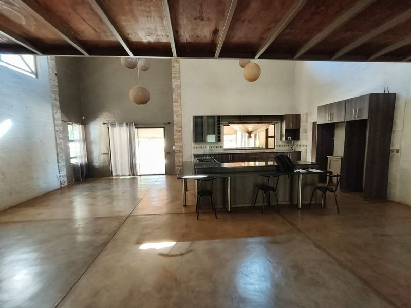 Spacious open-plan living and kitchen area featuring polished concrete floors, exposed timber beam ceilings, and a modern kitchen island with built-in cabinetry.