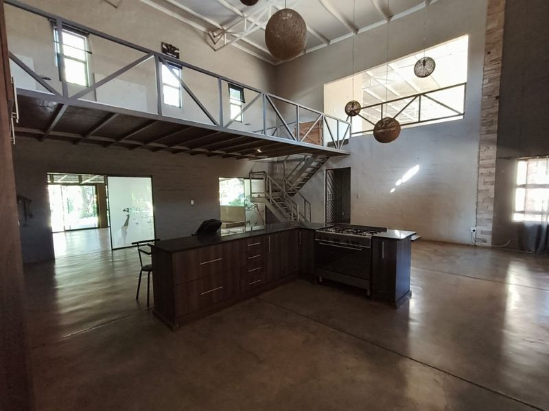 Spacious open-plan living area featuring polished concrete floors, a modern kitchen island with gas stove, and a mezzanine level with metal staircase.