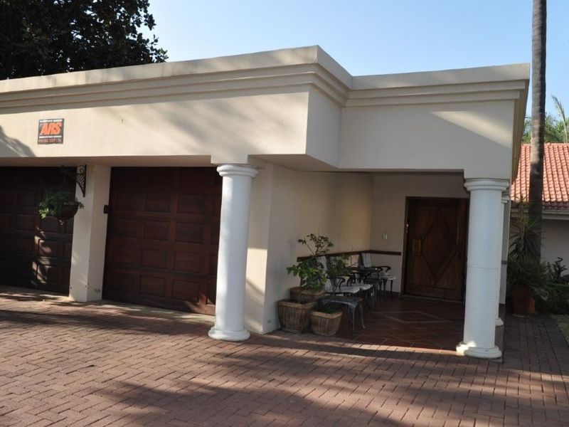 Front elevation featuring a double garage with timber doors, a covered entrance porch with decorative columns, and a paved driveway.