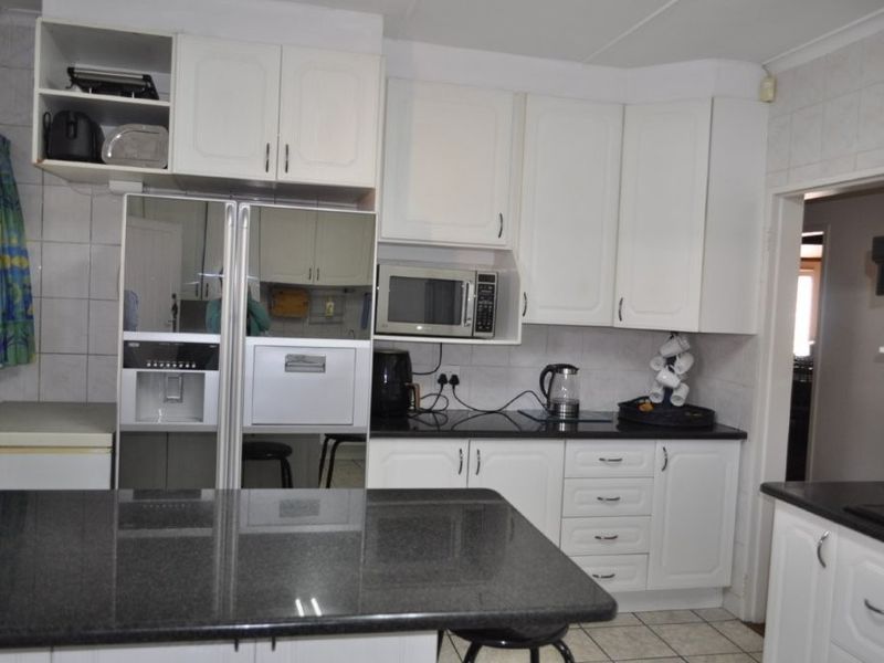 A functional kitchen featuring white cabinetry, dark granite countertops, tiled backsplash, and tiled flooring, providing a clean and practical workspace.