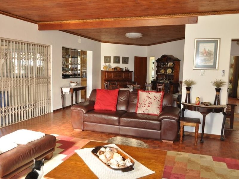 Spacious living room featuring warm parquet flooring and a distinctive timber ceiling, with an adjacent built-in bar area and secure sliding gate access.