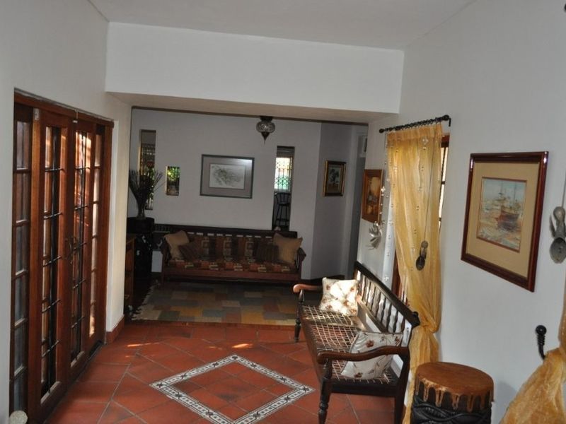 A living area featuring terracotta floor tiles with a decorative inlay and wooden framed glass doors leading to an adjacent space.