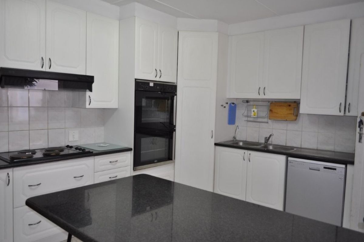 A functional kitchen featuring white cabinetry, a double wall oven, electric hob, and a dark granite island countertop with ample workspace.