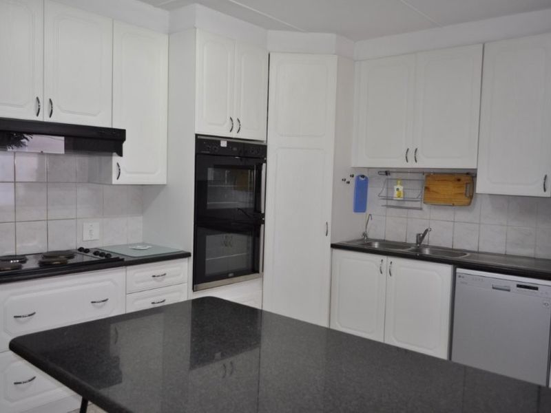 A functional kitchen featuring white cabinetry, a double wall oven, electric hob, and a dark granite island countertop with ample workspace.