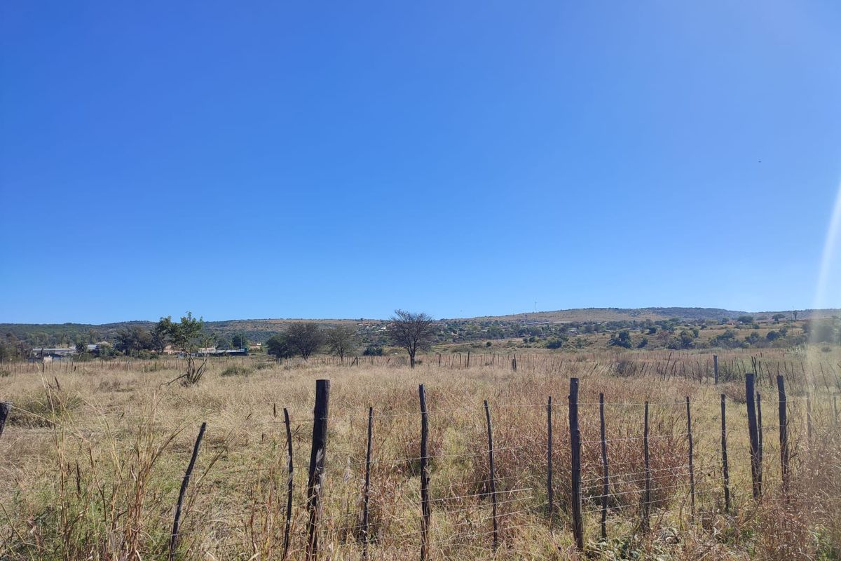 A view of a vacant residential plot featuring natural grass landscape and perimeter wire fencing with wooden posts under a clear blue sky.