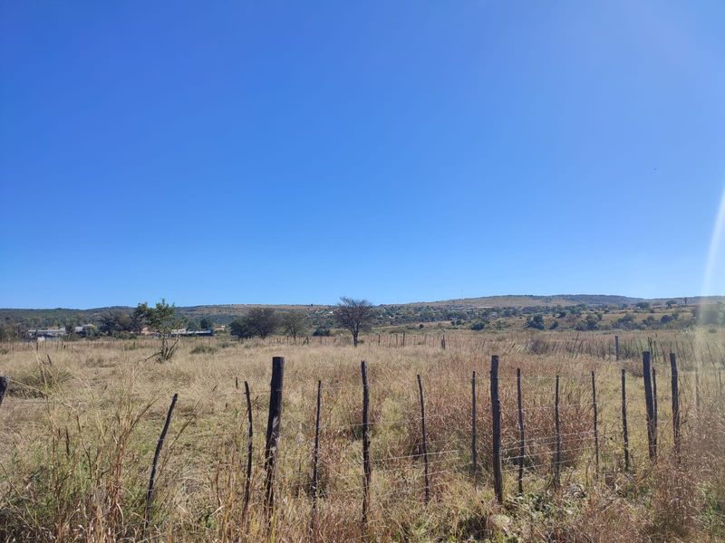 A view of a vacant residential plot featuring natural grass landscape and perimeter wire fencing with wooden posts under a clear blue sky.